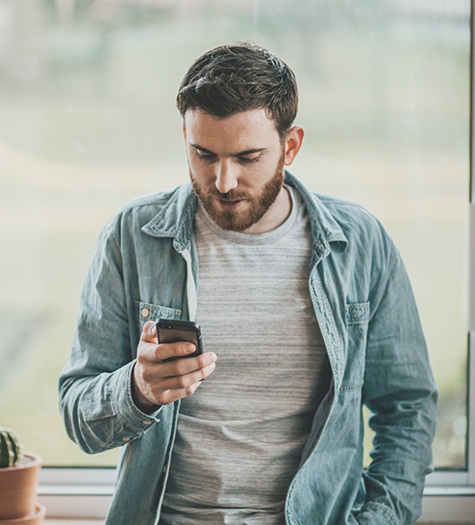 Man leaning against a window ledge looking at his phone