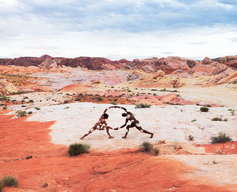 Two male figures in dessert reach out to each other