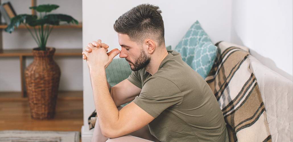 Photo of a man sitting on a couch with his hands in a thinking position on his head