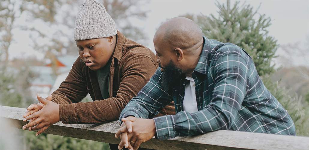 A father and son leaning over a fence having a somber discussion